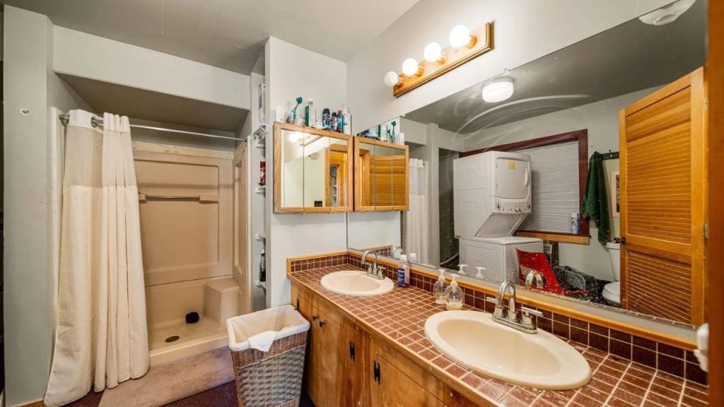 Rustic bathroom with double sinks, a shower, and a stacked washer and dryer.