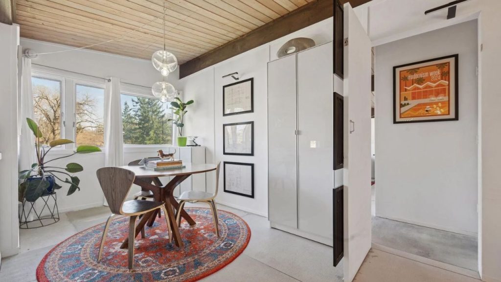 Bright home office with round wood table, midcentury chairs, and colorful rug.