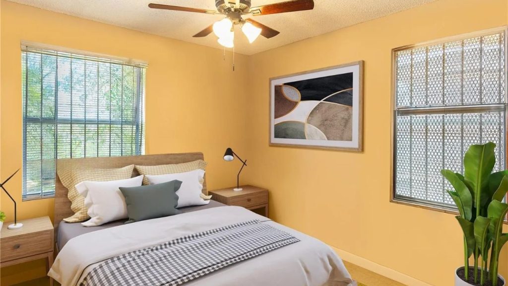 A cozy bedroom with yellow walls, a bed with checkered throw, black lamp, potted plant, and abstract art.