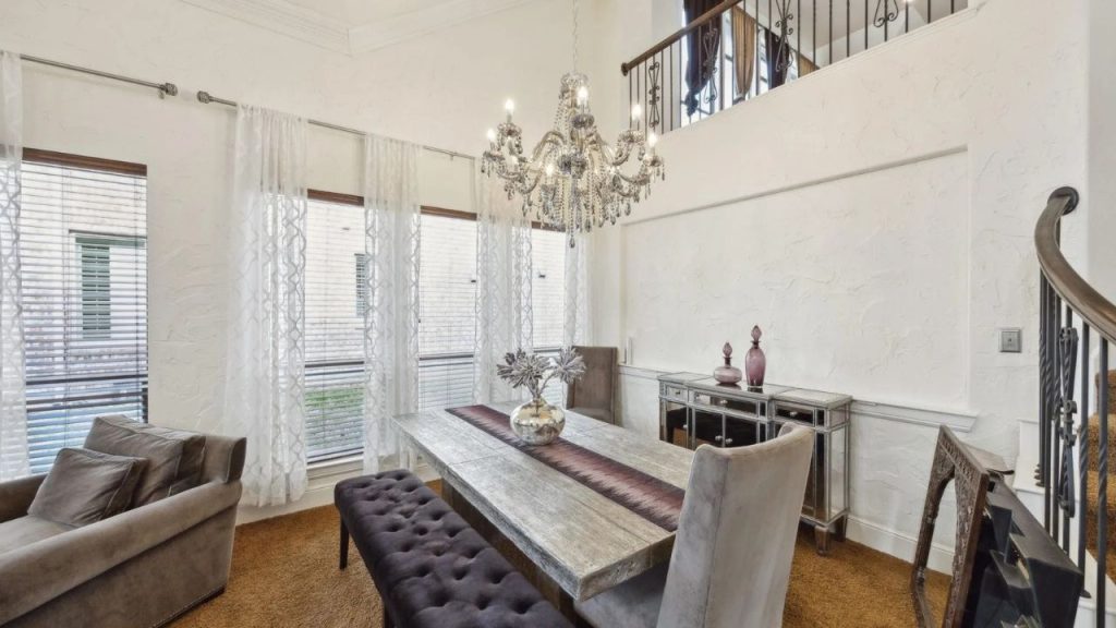 Bright dining room with chandelier, wooden table, and tall windows.