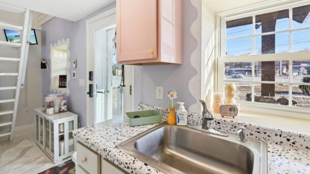 Bright kitchen sink area with terrazzo countertops and pastel pink cabinet.