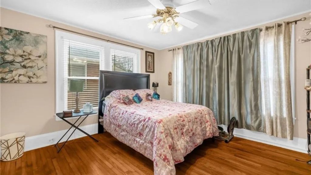 Bright bedroom with hardwood floors, floral bedding, and soft green curtains.