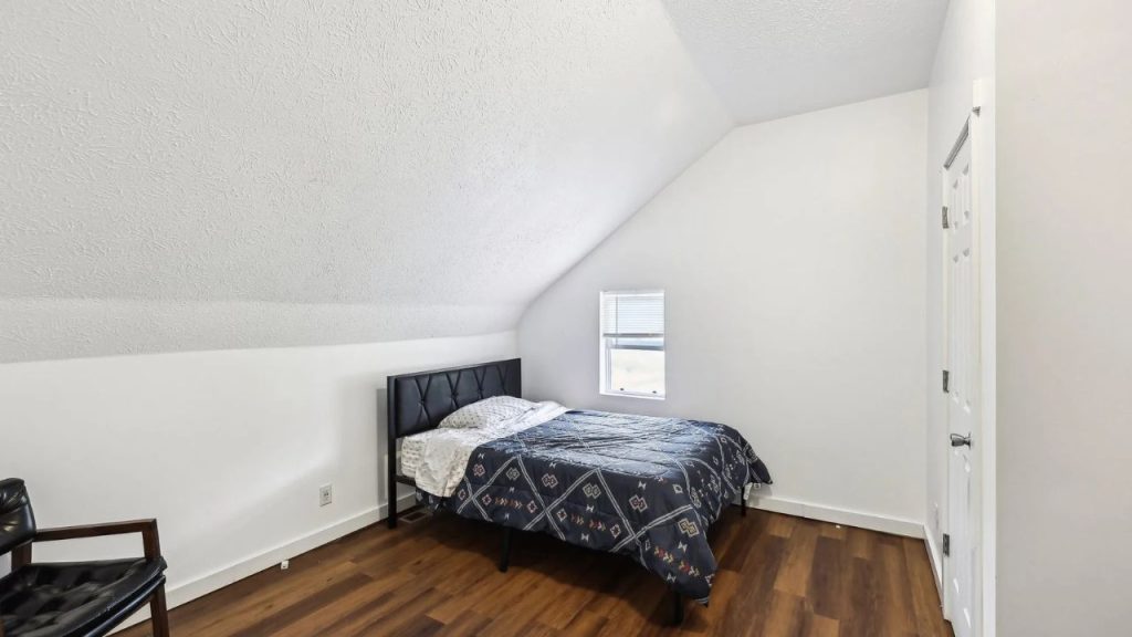 Small attic bedroom with angled ceiling, black headboard, and wood floors.
