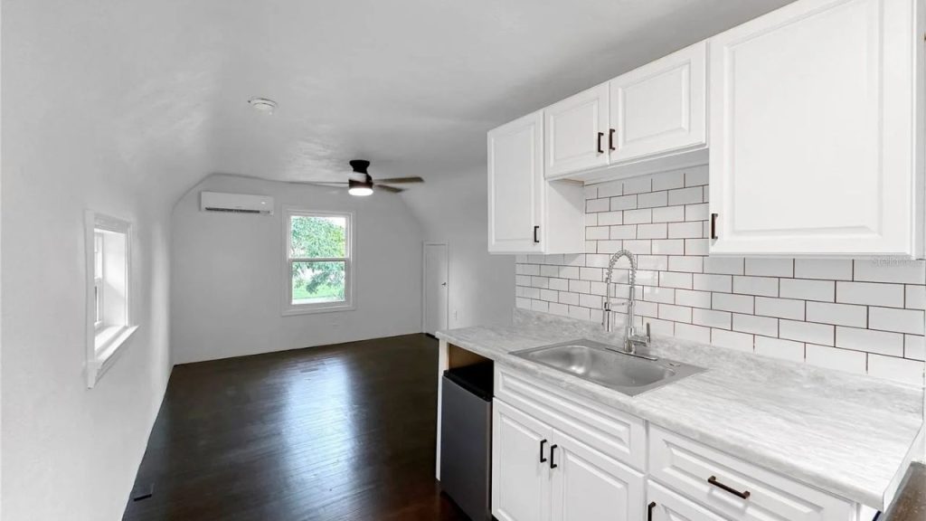 Compact white kitchenette with subway tiles and dark wood floors.