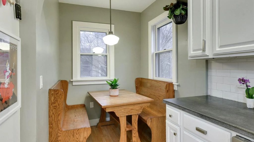 Cozy kitchen breakfast nook with wood benches, pendant light, and windows.