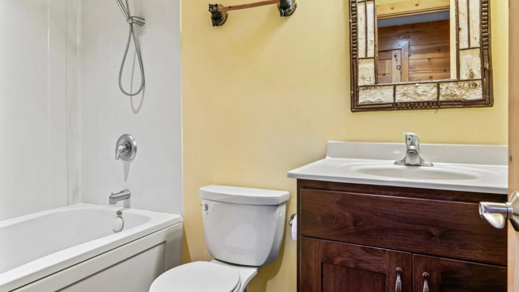 Cozy bathroom with rustic mirror, dark vanity, and bear-themed towel rack.