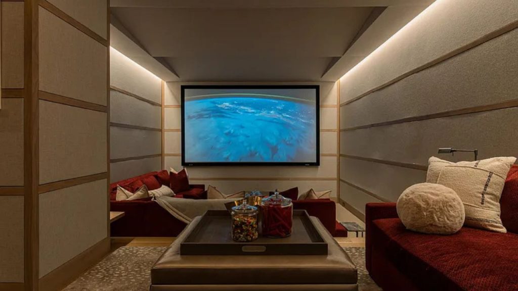 A cozy home theater with red sofas and a large screen showing an underwater scene.