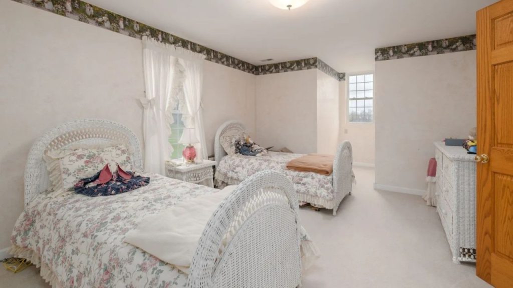 A cozy bedroom with twin beds, floral bedding, wicker furniture, and soft natural light.