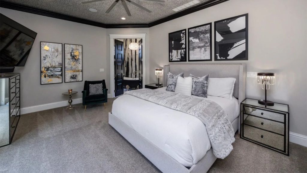 A cozy bedroom with a plush bed, mirrored nightstands, bold artwork, and a ceiling fan, creating a serene and stylish haven.