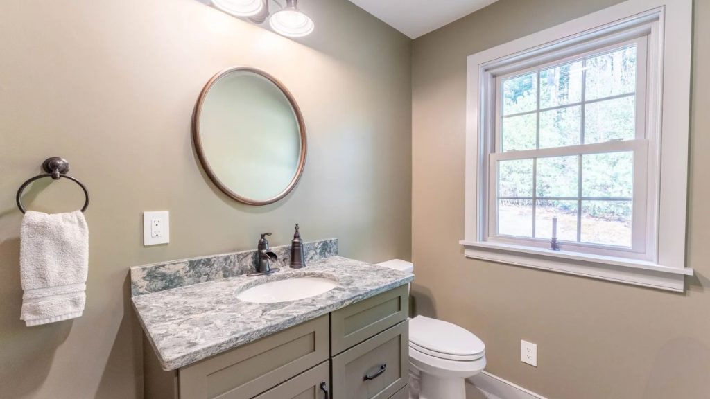 Warm-toned bathroom with a green vanity, marble countertop, and large window.