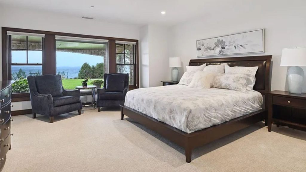 A serene bedroom with a lake view, dark wood bed, and blue armchairs.