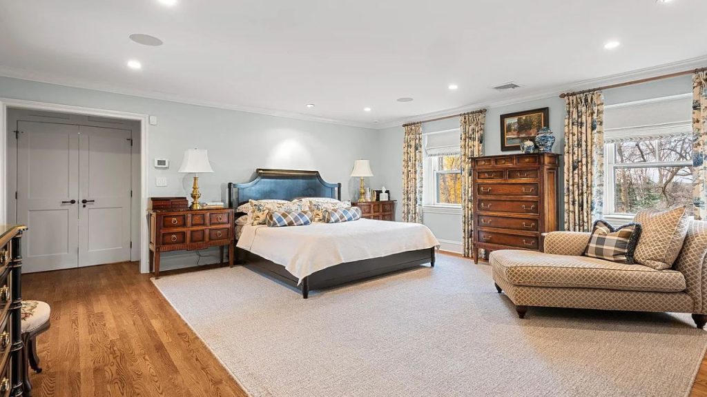 A tranquil bedroom with a blue headboard, large windows, and a chaise lounge.