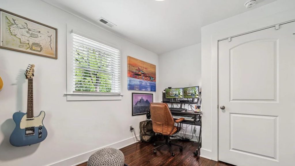 A workspace with a desk, dual monitors, guitar, and artwork on the wall.
