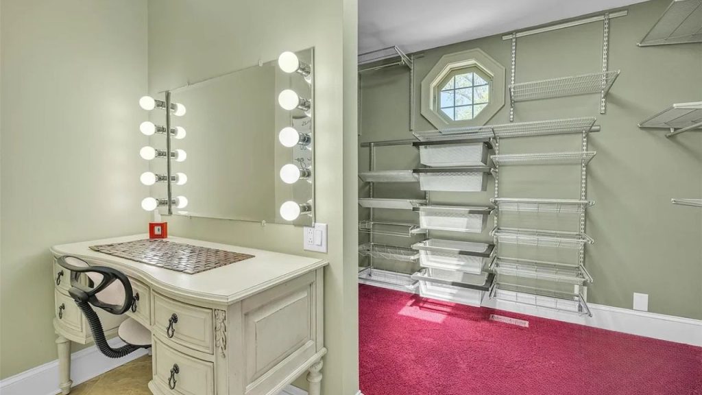 A stylish dressing room with a lit vanity mirror, green walls, and a closet with red carpet and shelving.