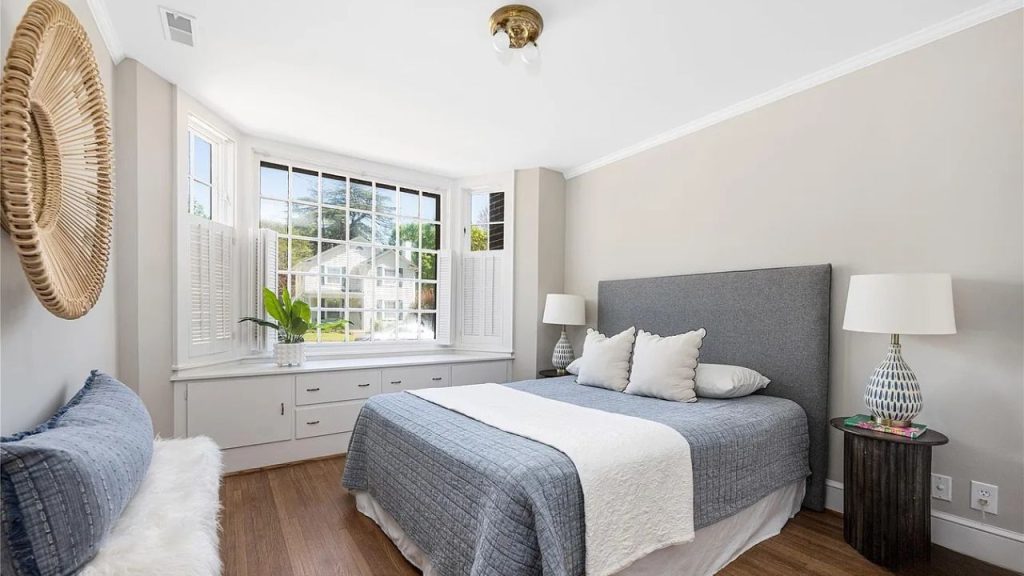 A bright bedroom with a bay window, blue bed, and woven wall decor.