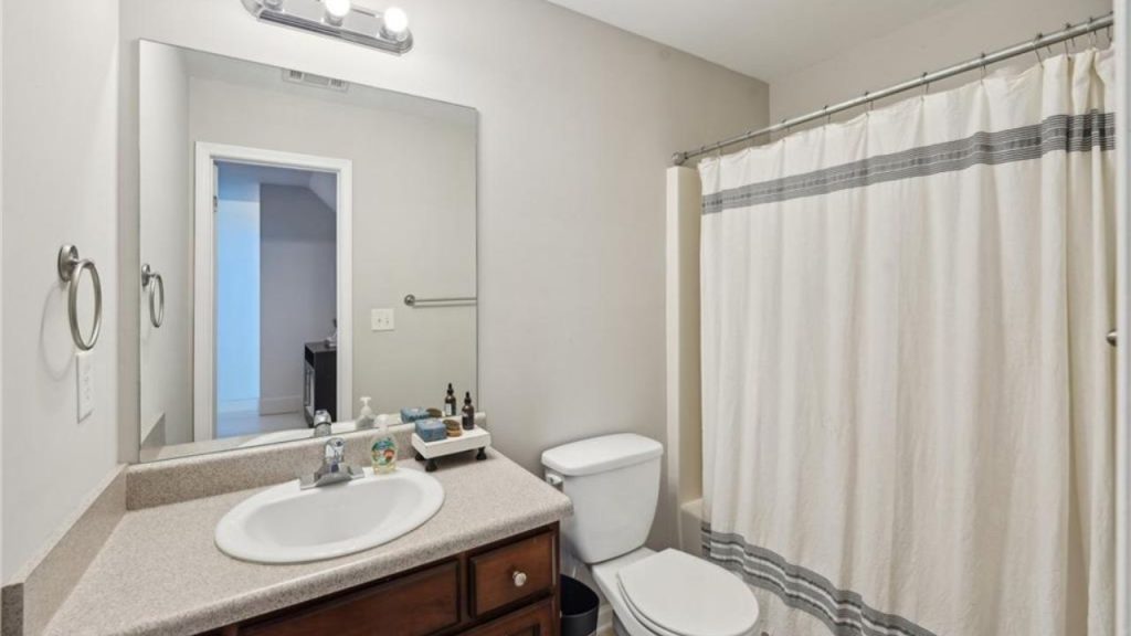 A simple bathroom with a mirror, sink, toilet, and shower curtain in a neutral space.