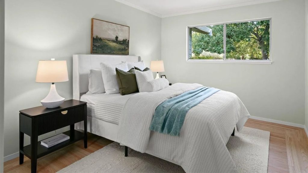 A tranquil bedroom with a white bed, green accents, and a large window overlooking trees.