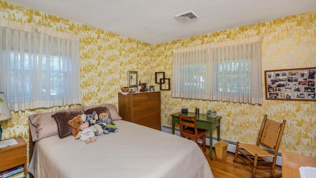Sunny bedroom with vintage wallpaper, green desk, and plush toys on the bed.