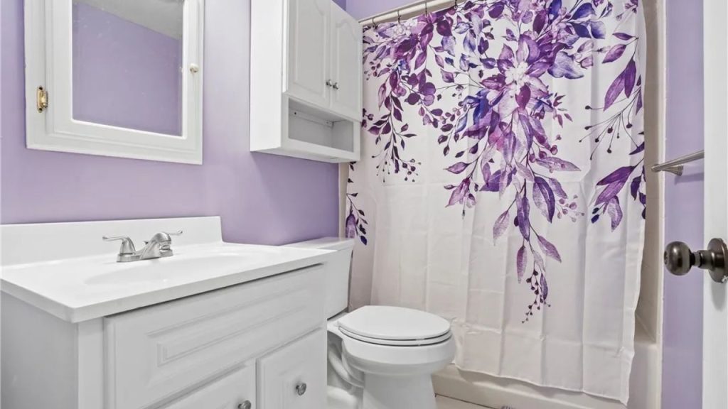 Lavender bathroom with white vanity and purple floral shower curtain.