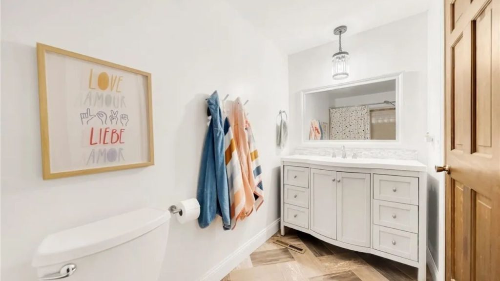 Bright bathroom with white vanity, colorful towels, and framed wall art.
