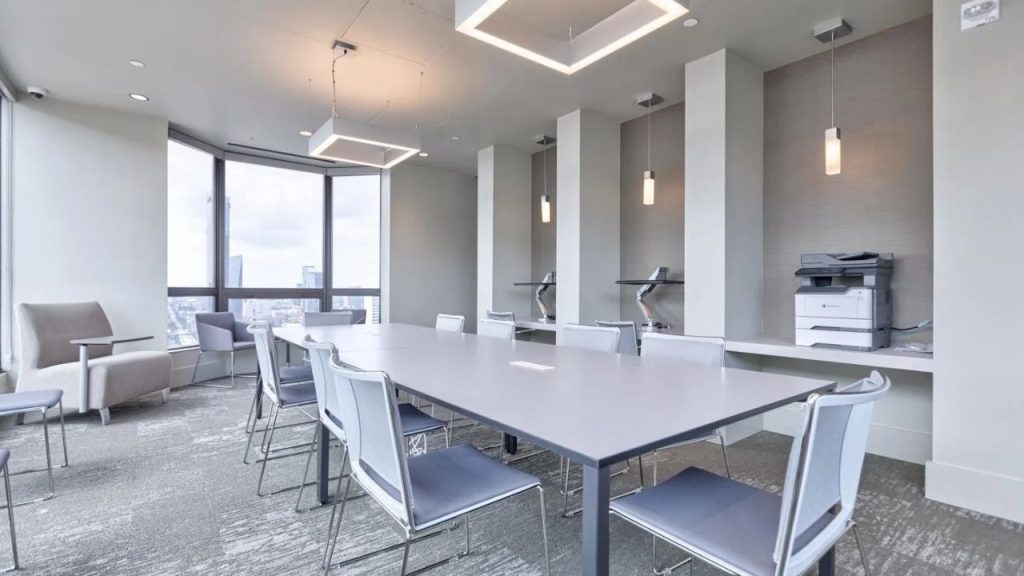 Modern office room with large windows, a long table, and built-in workstations.