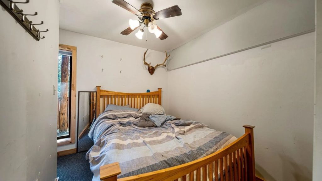 Small rustic bedroom with wooden bed, antlers on wall, and forest view.