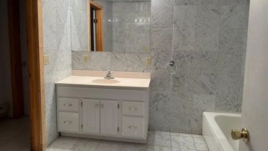 Bright marble bathroom with white vanity and large mirror.
