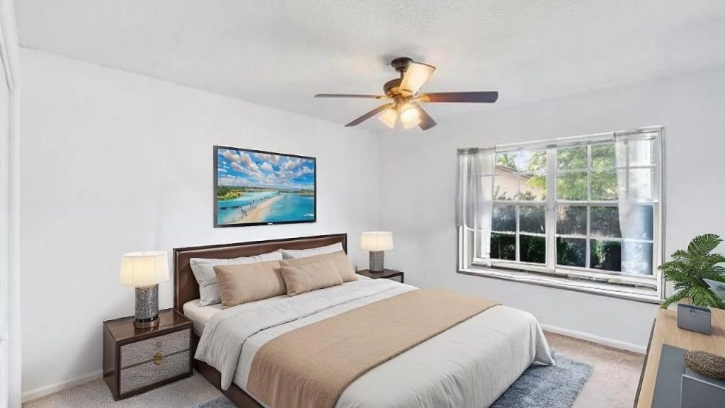 A calm bedroom with a beige throw, coastal art, and large windows.