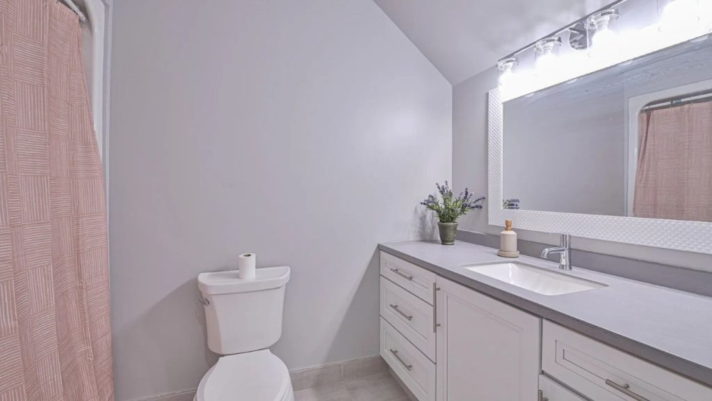 Modern bathroom with soft gray tones, white cabinetry, and a blush shower curtain.