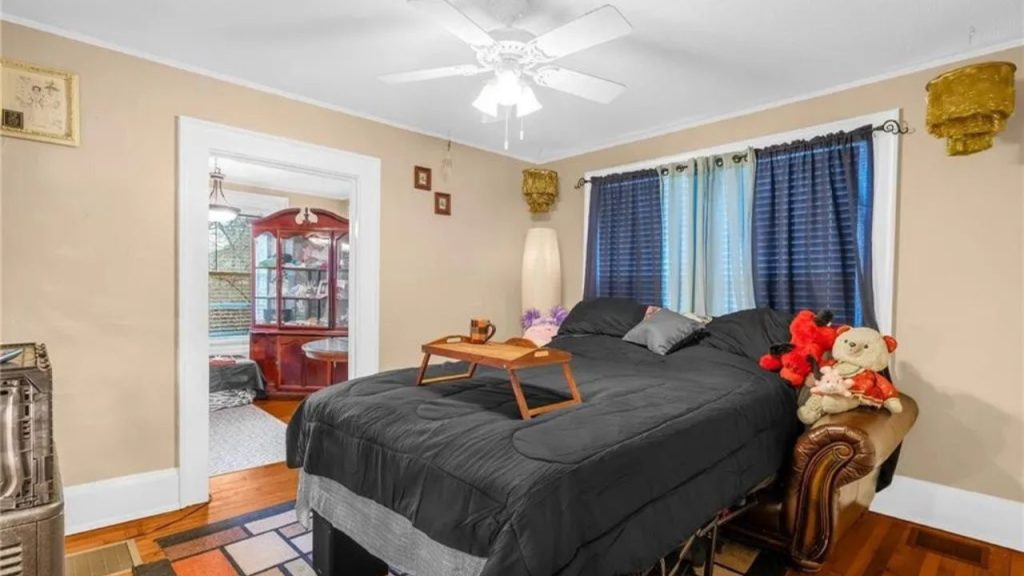 Cozy bedroom with dark bedding, plush toys, and view into the dining area.