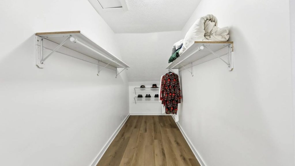 Long walk-in closet with white shelves, wood floor, and a sloped ceiling.