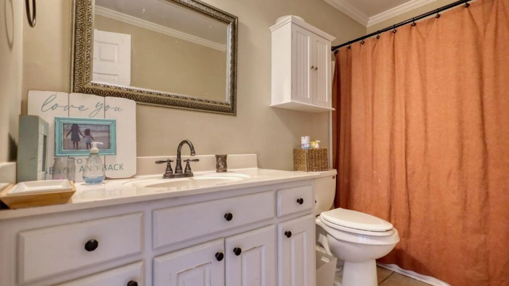 Guest bathroom with white vanity, bronze fixtures, and warm-toned shower curtain.