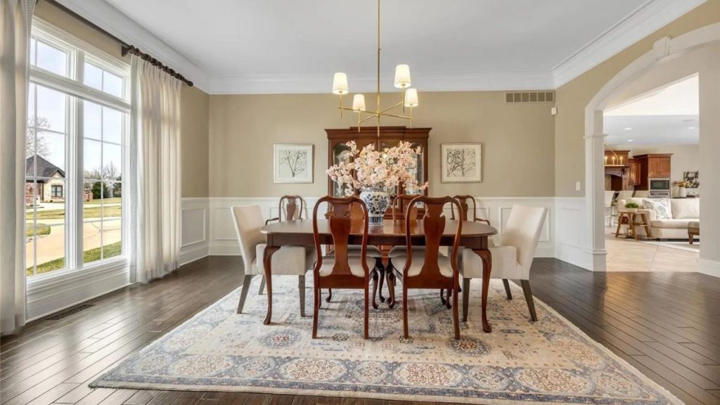 A bright and elegant dining room with a wooden table, upholstered chairs, and a modern chandelier.