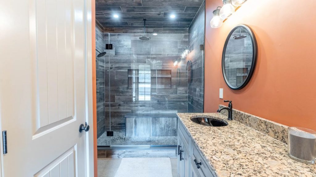 Modern bathroom with orange walls, a granite vanity, and a glass-enclosed shower.