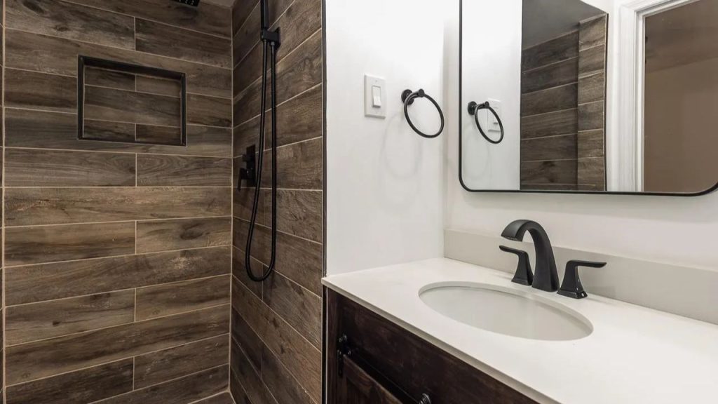 A rustic bathroom with wood-look tiles, a modern vanity, and a shower with a handheld sprayer.