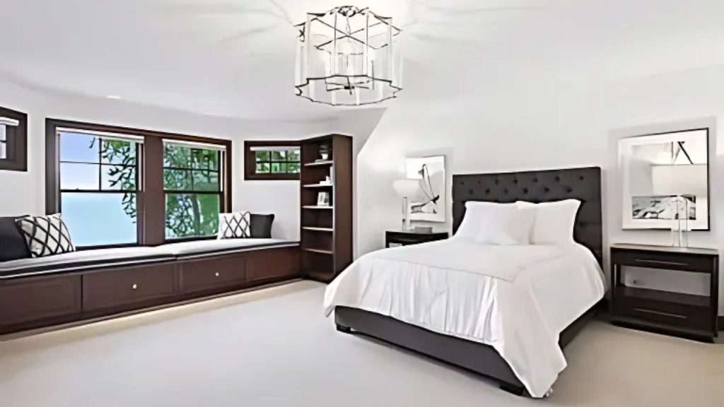 A cozy bedroom with a window seat, chandelier, and dark wood bed.