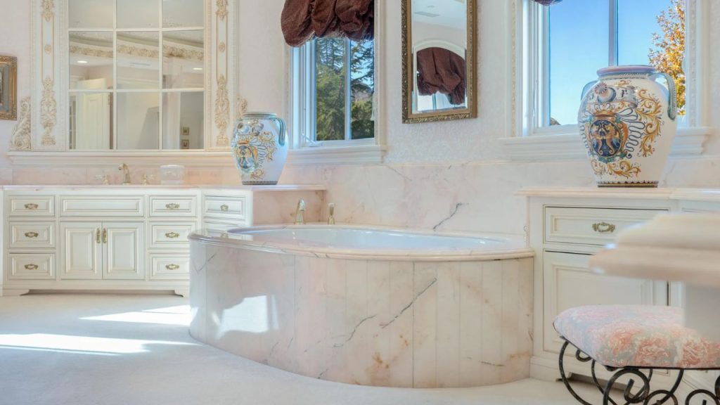 A luxurious bathroom with a marble tub, ornate vases, and tall windows.