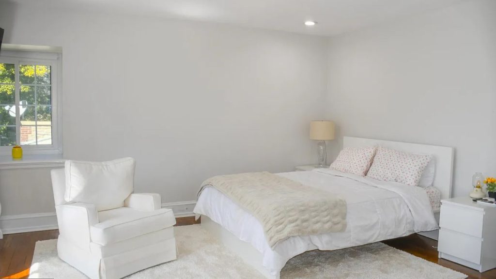 A peaceful bedroom with a white bed, armchair, and sliding glass door on a shaggy rug.