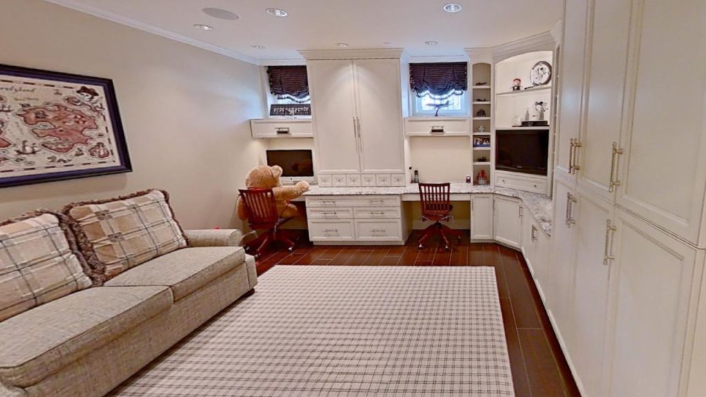A cozy kid’s room with a sofa, desk, white cabinets, and a checkered rug, featuring a map and teddy bear.