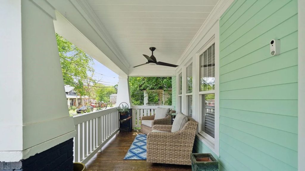 A mint-green porch with wicker chairs, a ceiling fan, and large windows.
