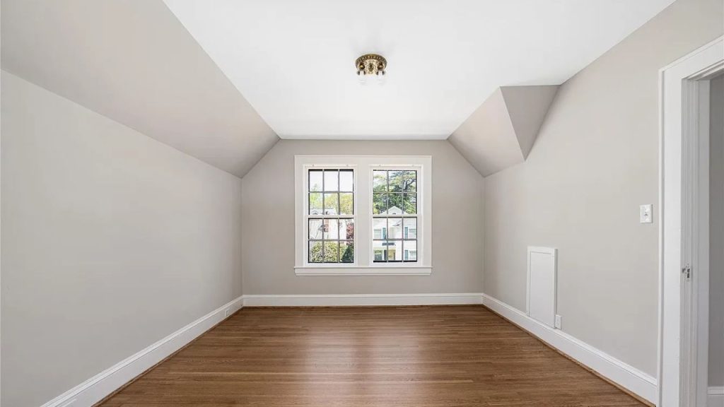 A bright bedroom with large windows, hardwood floors, and a slanted ceiling.