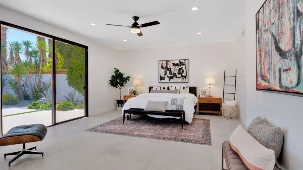 A serene bedroom with a white bed, abstract art, and views of a desert garden.