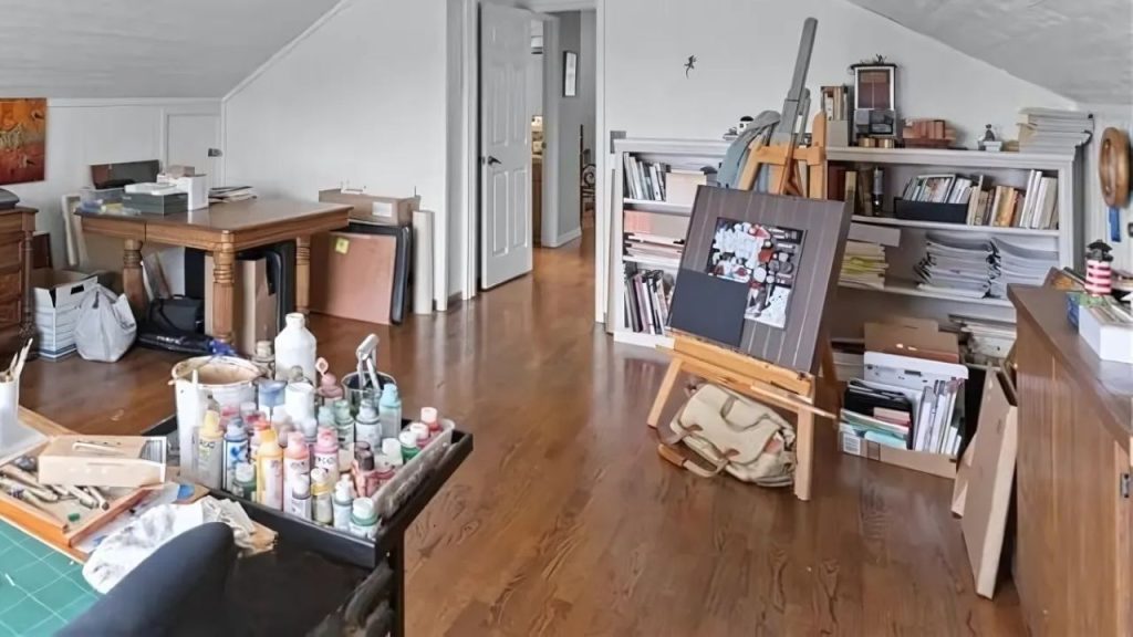 A creative art studio with an easel, wooden table, shelves of supplies, and warm hardwood floors.