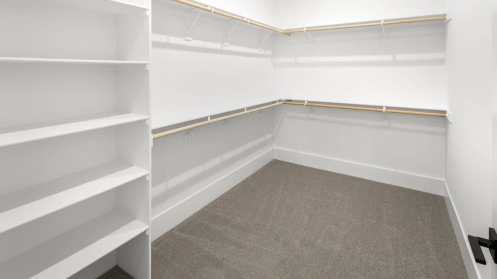 A primary closet with white shelving, wooden rods, and gray carpeting, offering ample storage space.
