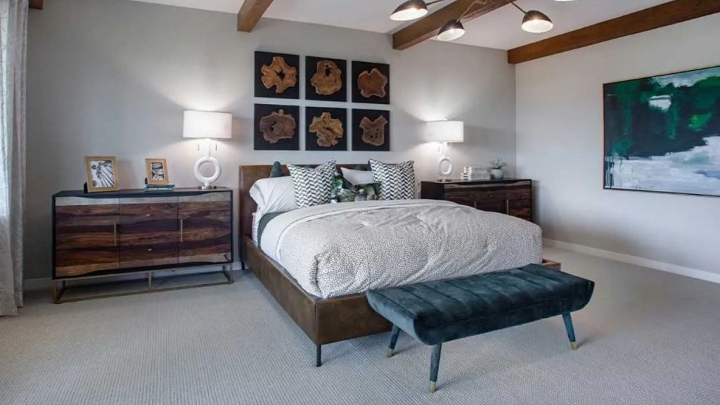 A spacious master bedroom with a plush bed, wooden dressers, exposed beams, and abstract wood art on the wall.