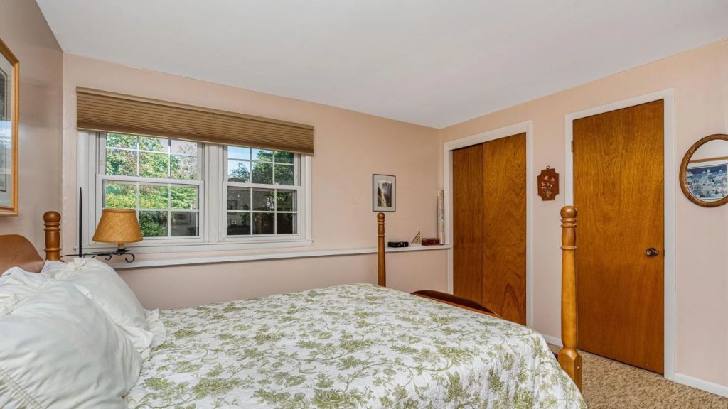 Calm bedroom with wood furniture, leafy bedspread, and large windows.