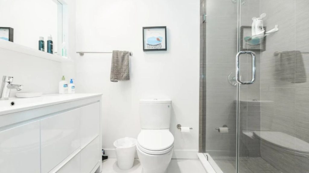 Minimalist bathroom with white vanity, glass shower, and wall art.