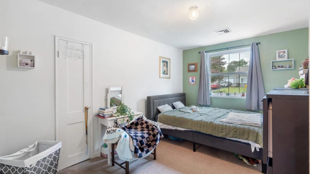 Light-filled bedroom with green accent wall, gray bed, and personal touches.