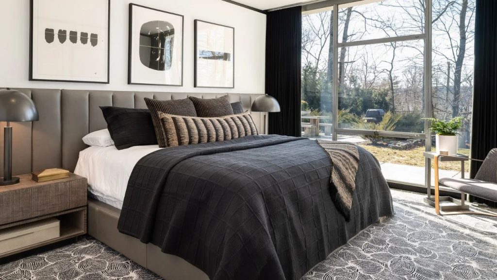Modern bedroom with dark bedding, large windows, and nature views.