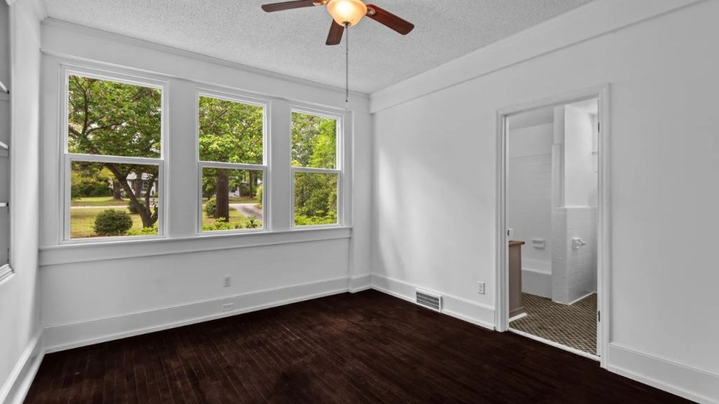 Bright bedroom with dark wood floors, large windows, and a door leading to a bathroom.
